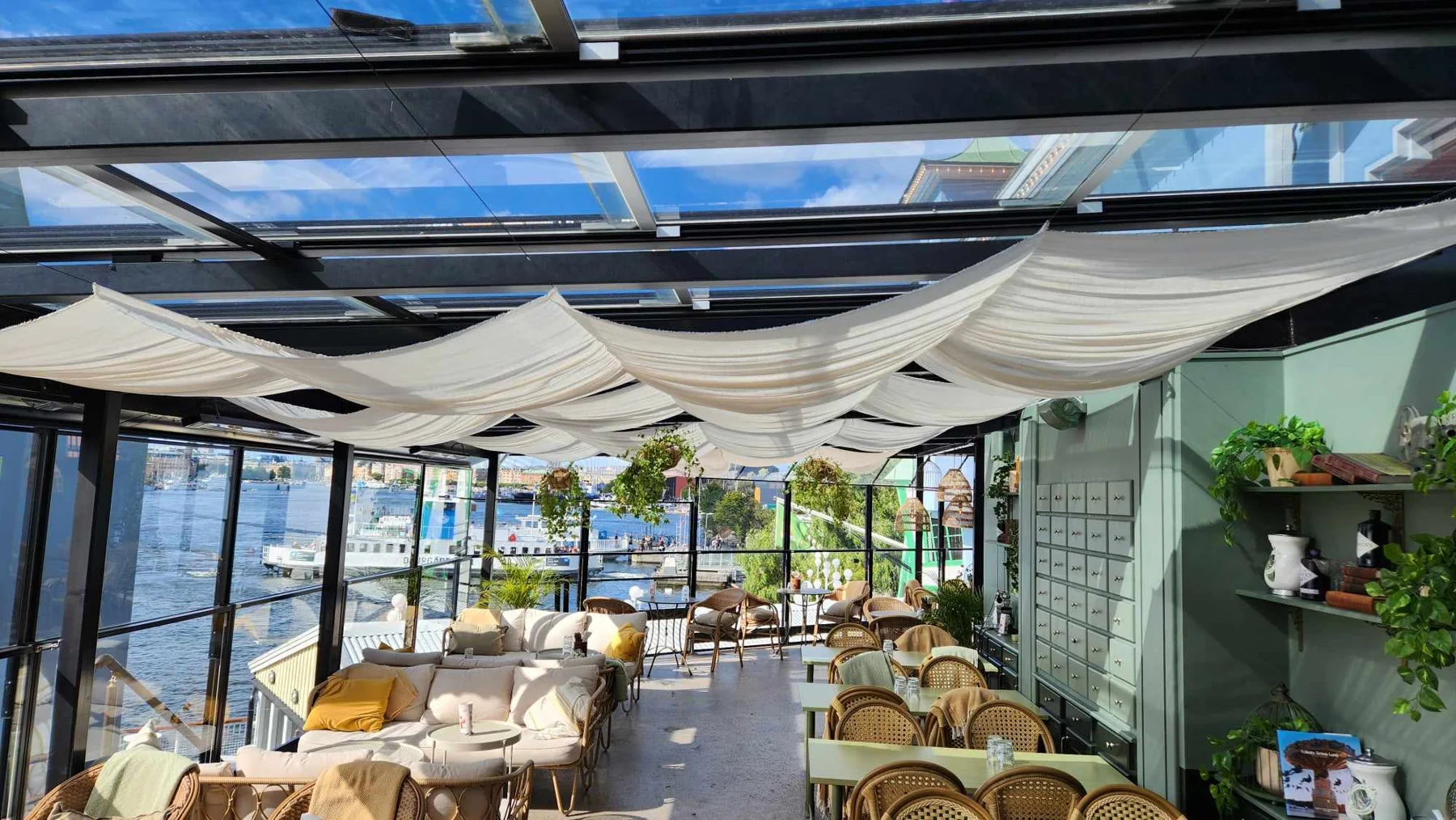 Dining area at Gröna Lund beneath the retractable glass roof, with light fabrics and waterfront views